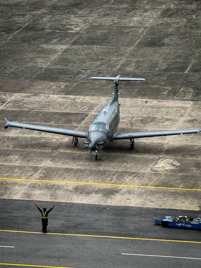 Aerial shot of a gray private jet with marshal signaling on runway.